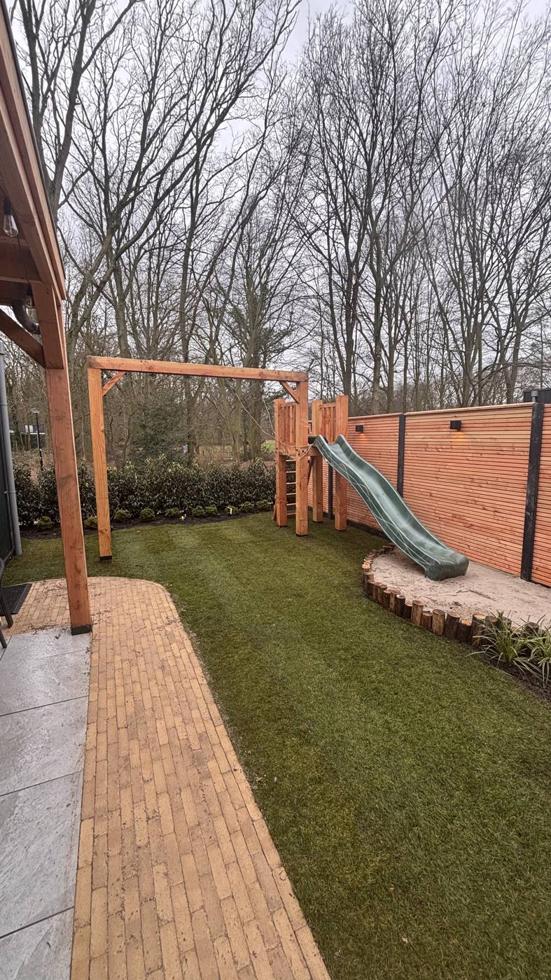 Speelgazon met glijbaan en bestrating naast de overkapping